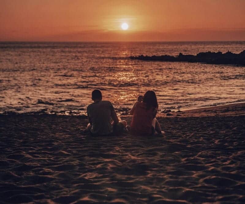 Two friends sitting on a beach at sunset, watching the sea