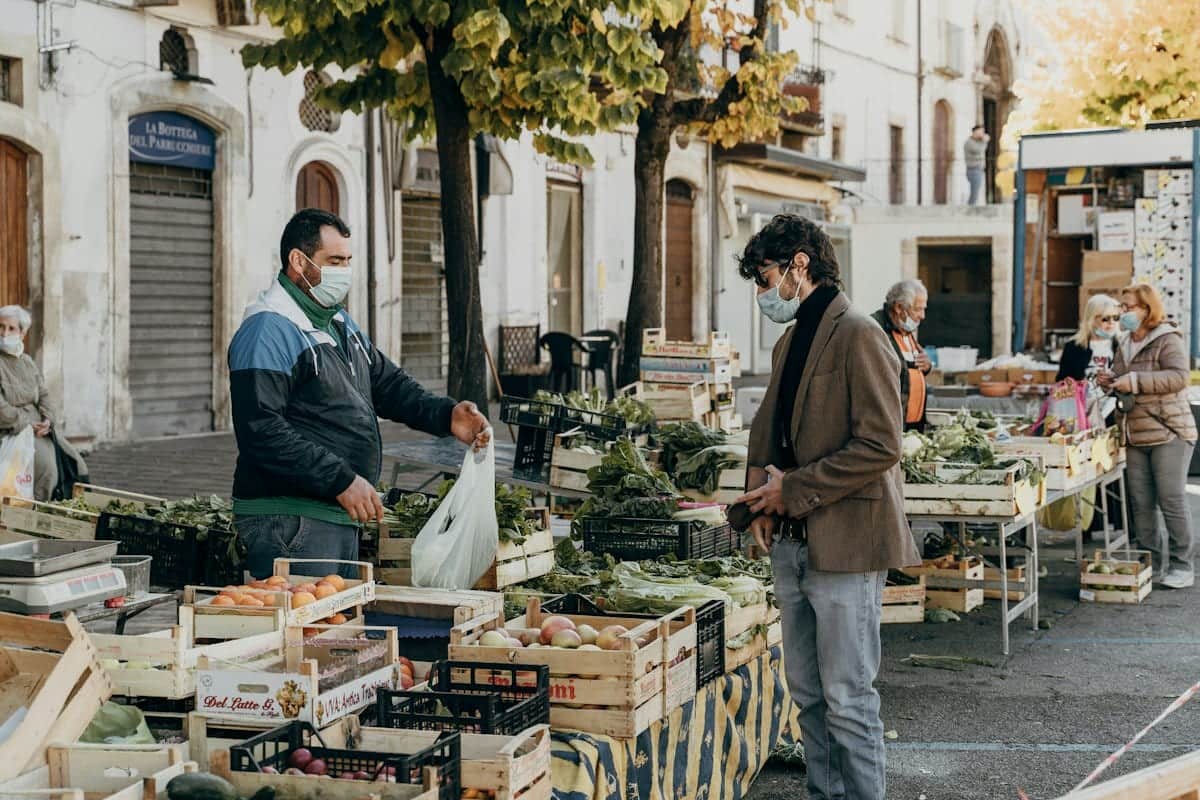 A stallholder serving a customer at an outdoor fruit and vegetable market