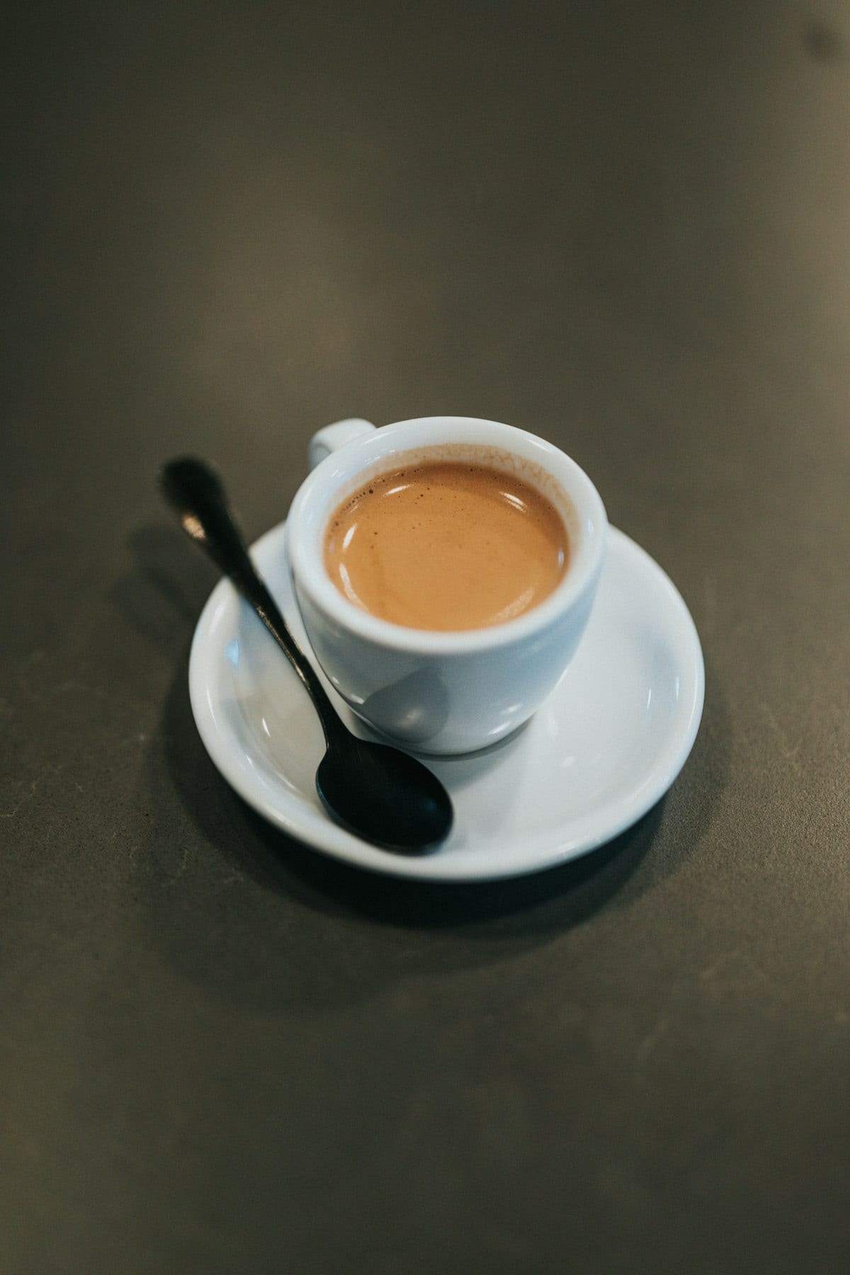 A small cup of coffee with a spoon on its saucer