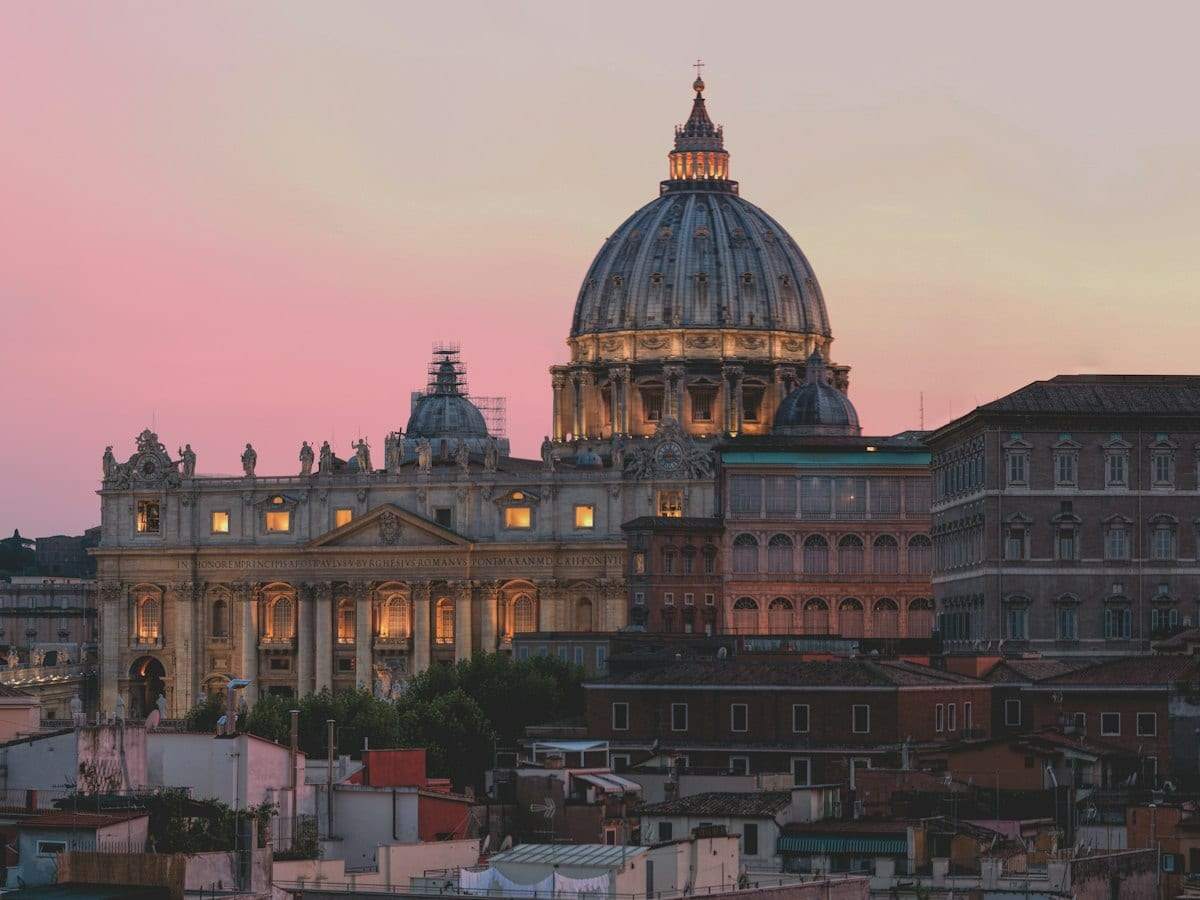 The dome of St Peter's in Rome lit up at dusk above the city's rooftops