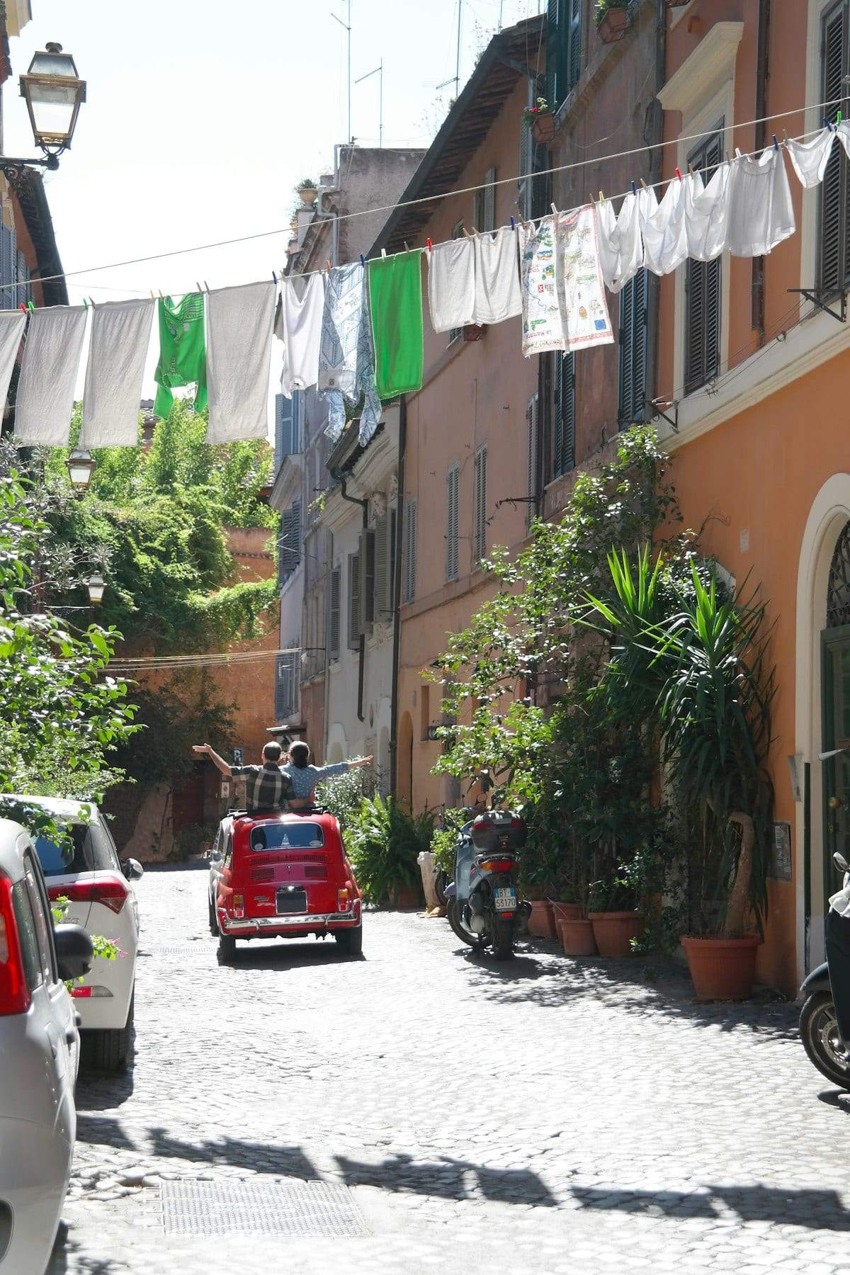 Washing hung on lines across a narrow street in Rome, with a small red car parked below