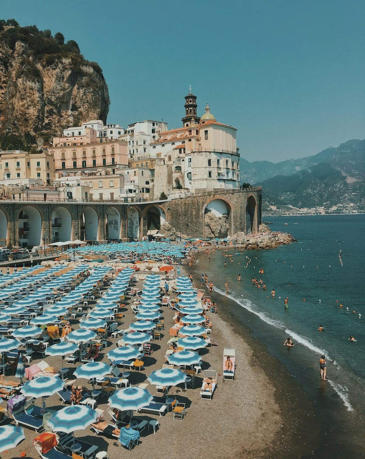 A crowded beach of blue umbrellas below a seaside town
