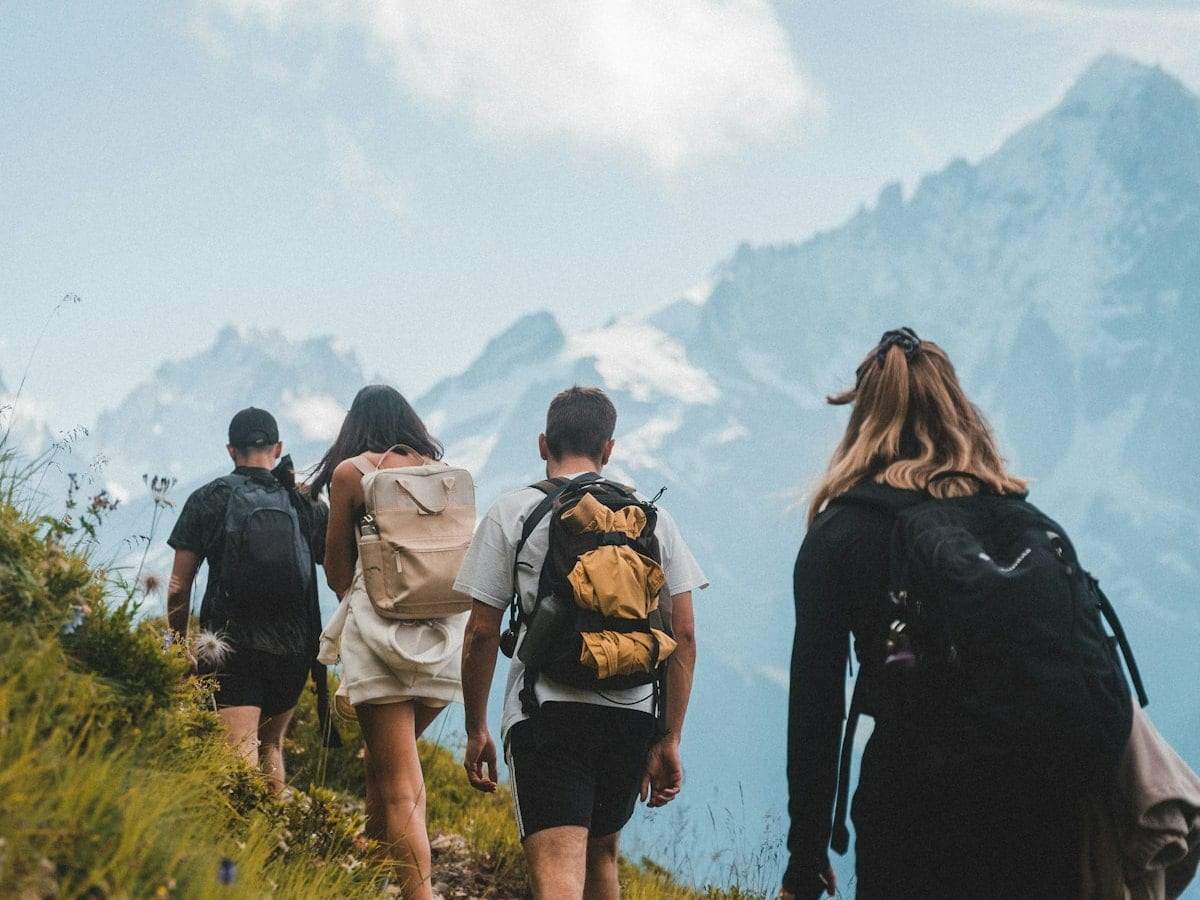 Four friends with backpacks walking up a mountain path together